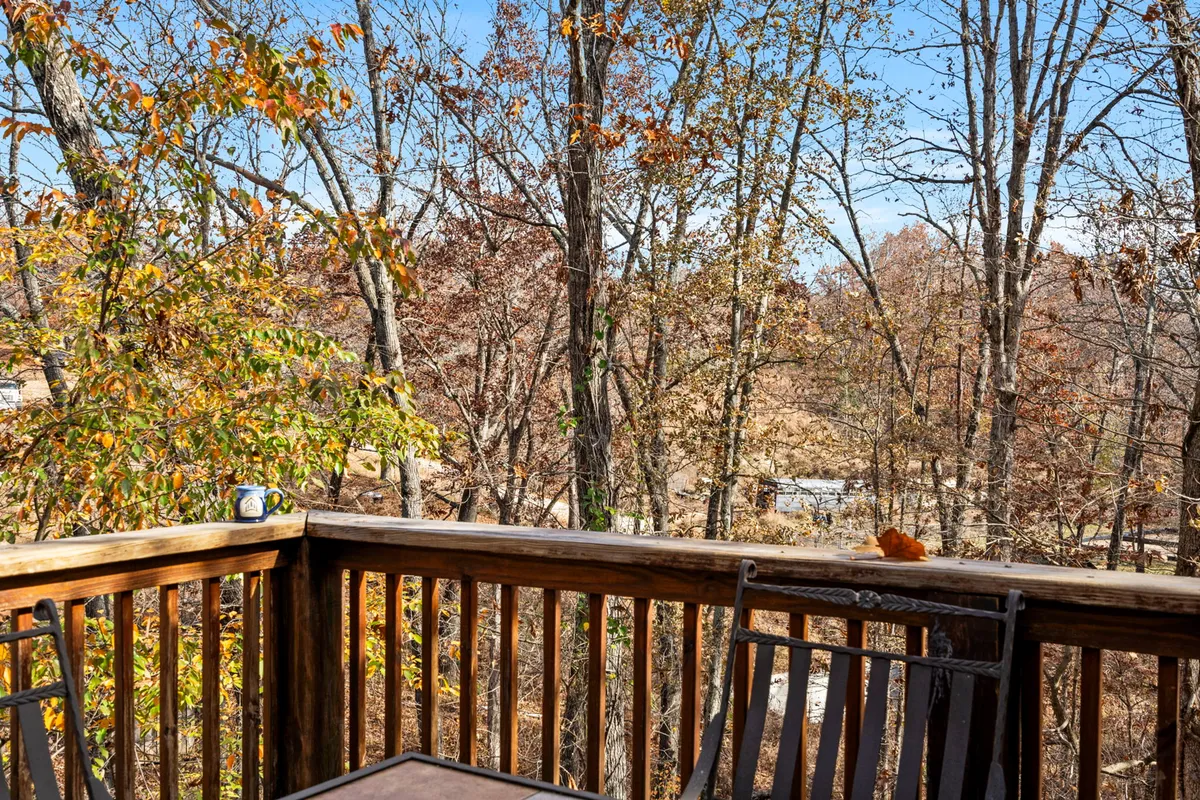 A tranquil deck view featuring a wooden railing and a table with a coffee mug, overlooking vibrant autumn foliage. The peaceful, natural setting invites guests to relax and take in the seasonal changes of the Ozarks.