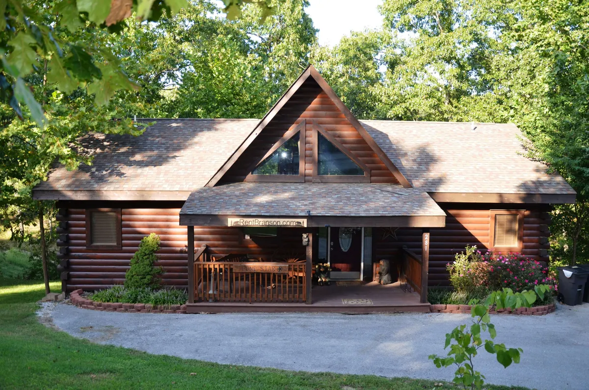 This exterior image features a cozy log cabin structure with a welcoming front porch adorned by flower beds and large windows. The inviting atmosphere is emphasized by the porch, perfect for relaxing and enjoying the surrounding nature.