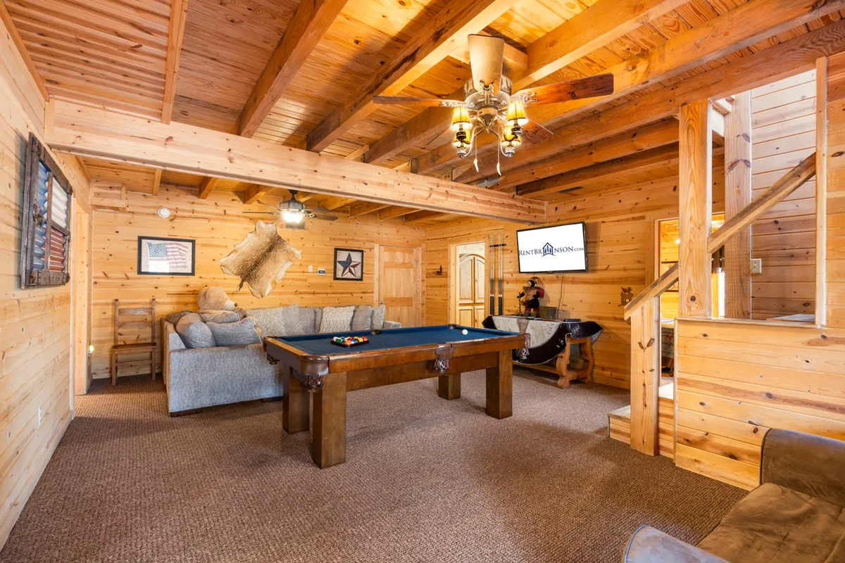A bright and playful recreation room with a pool table, plush sofa, chandelier, and a TV on the wall. The space exudes a relaxed and inviting atmosphere for both games and movie nights.