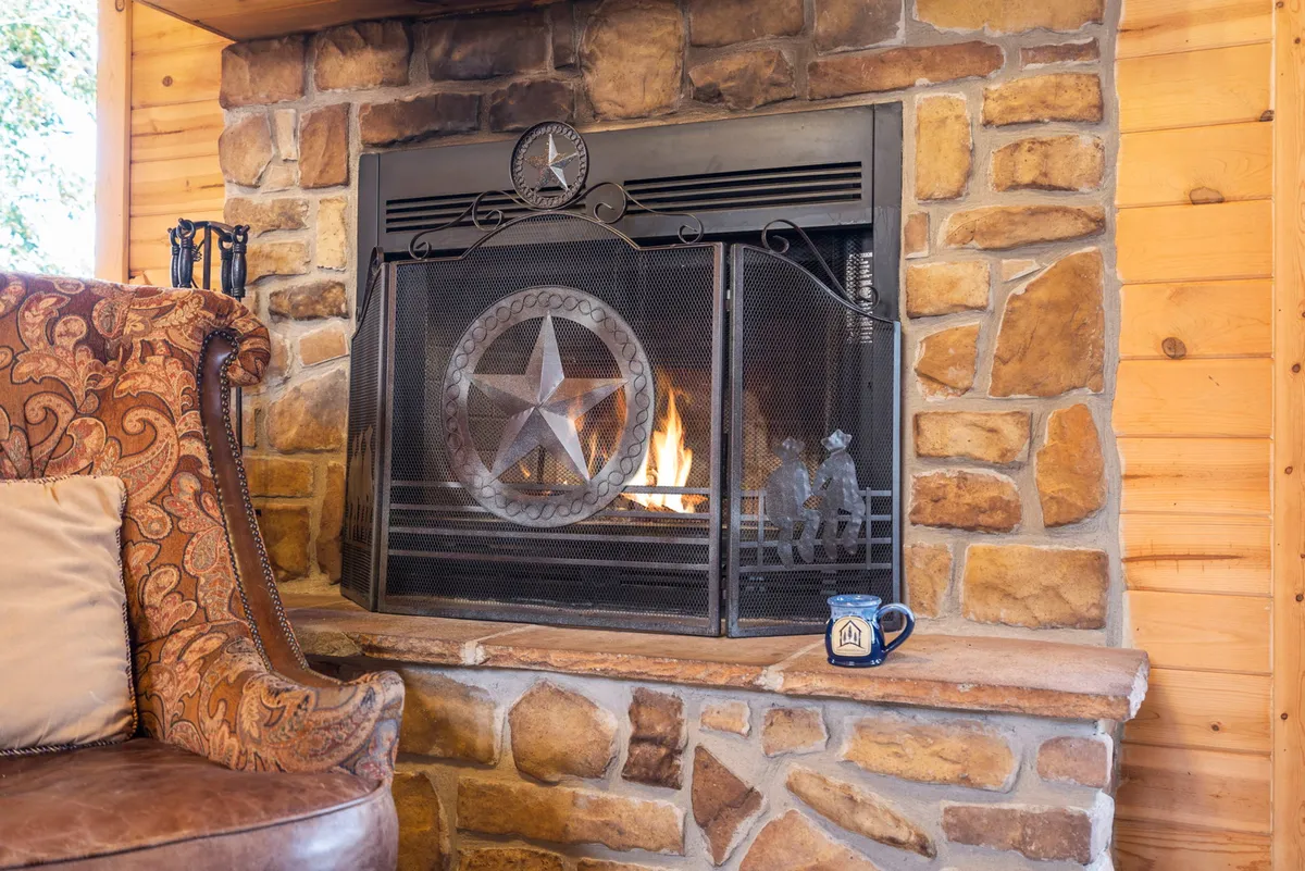 A cozy interior scene featuring a burning fireplace, a comfortable armchair, and a coffee mug placed within arm's reach. The warm, inviting atmosphere is perfect for unwinding during chilly evenings or winter stays.