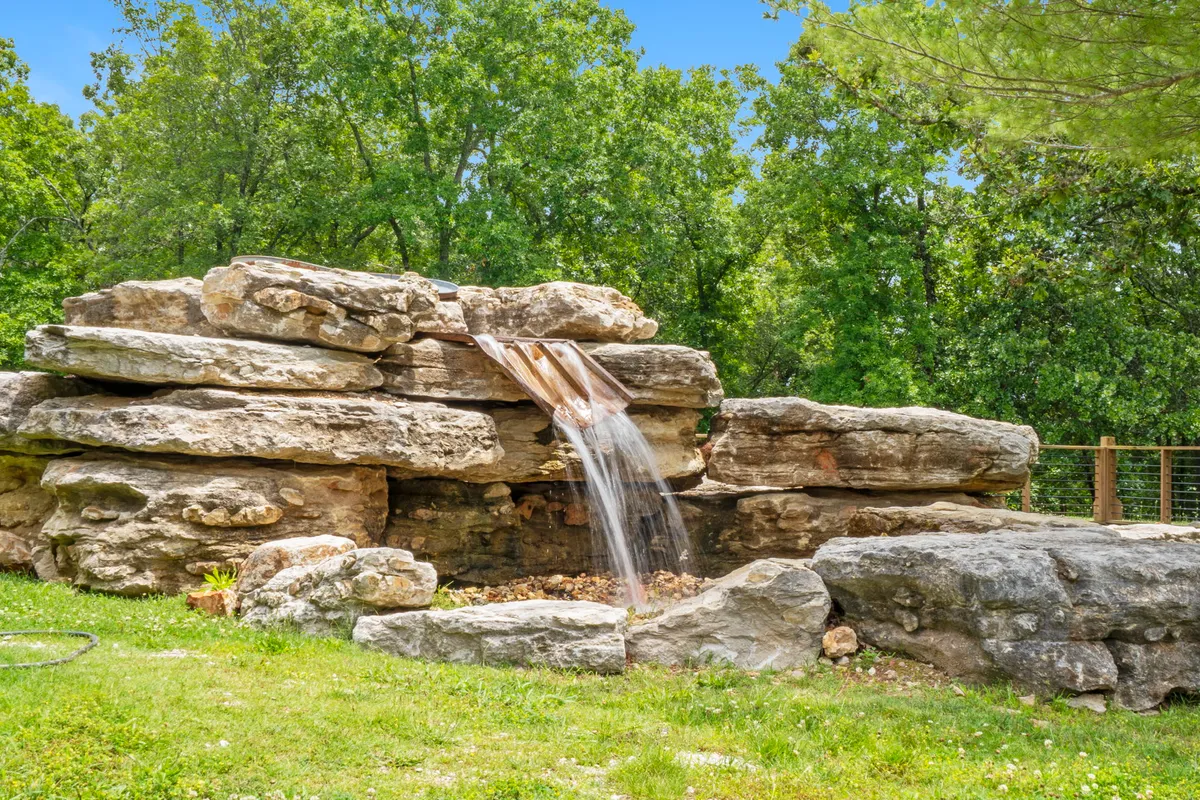 A serene scene featuring a natural rock formation and a waterfall surrounded by lush greenery. The area looks inviting for quiet reflection, birdwatching, or enjoying the gentle sounds of falling water.