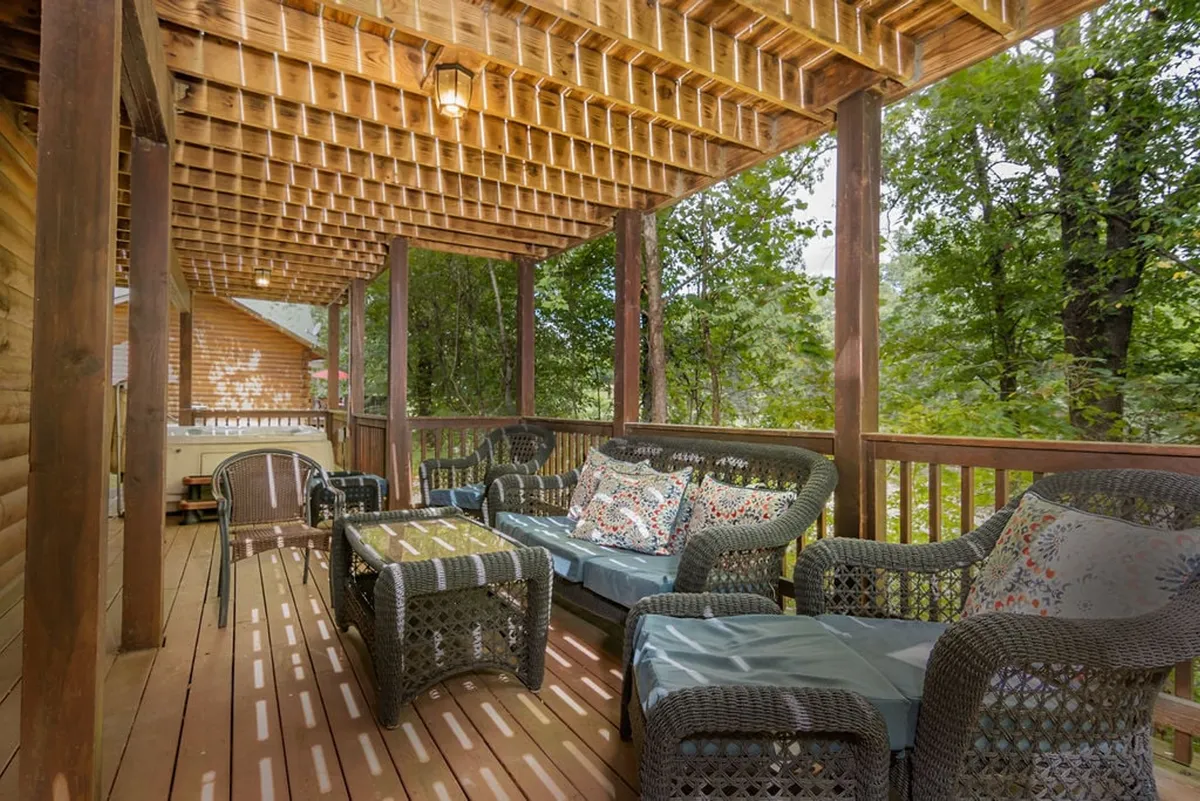 A cozy deck area with woven seating, decorative cushions, and a sturdy wooden railing. The setting offers a comfortable spot for enjoying nature and socializing, with hints of seasonal foliage and forest beyond the railing.