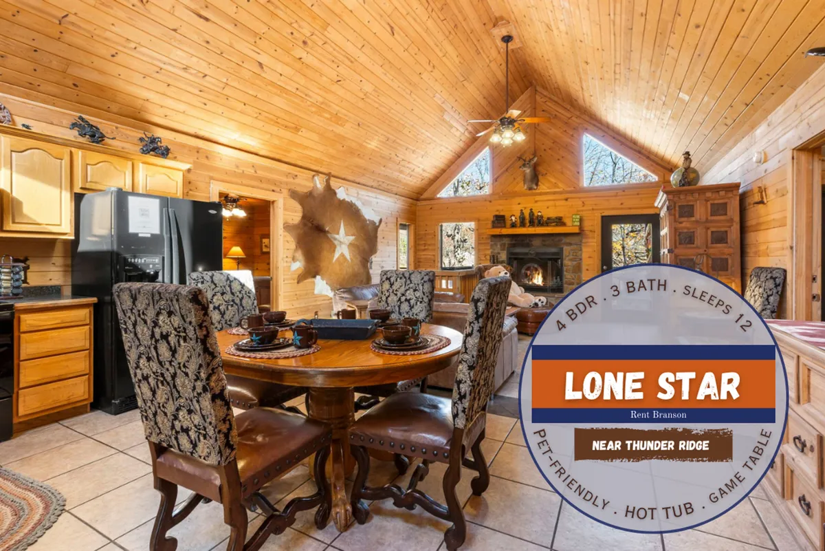 This image captures the dining table and kitchen area with a cozy wood-burning fireplace, wooden ceiling, and decorative wall art. The layout shows the spaciousness and open flow between the dining and kitchen spaces, inviting guests to gather around the table or enjoy warmth by the fire.