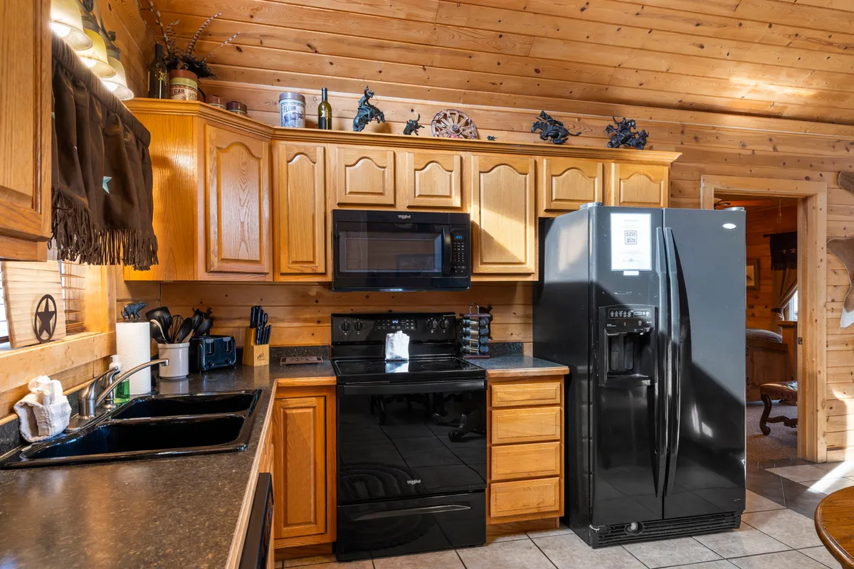 A view of the well-equipped kitchen featuring a black refrigerator, wooden cabinets, stainless steel appliances, and generous counter space. The scene implies readiness for meal preparation and the ability to host large gatherings.