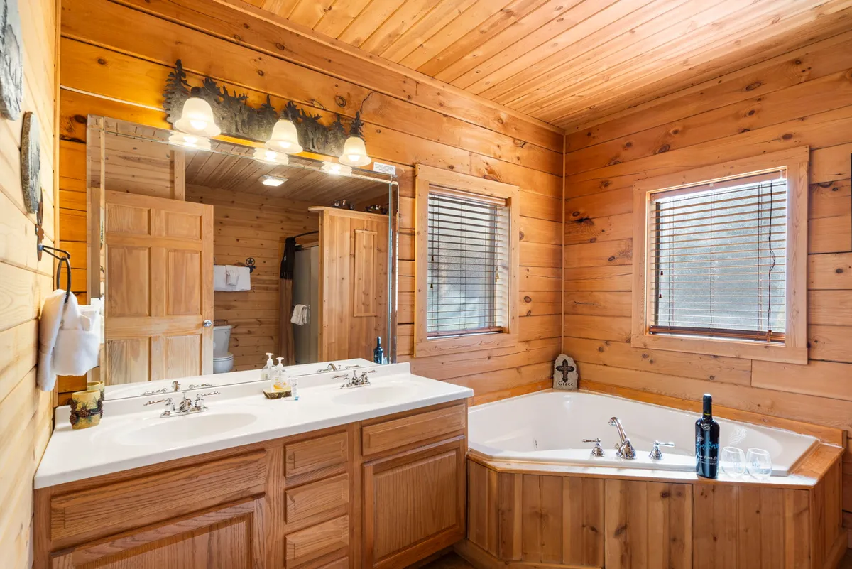 A luxurious bathroom featuring a double vanity sink, a large jacuzzi tub, and a sizable mirror, all complemented by inviting wooden accents and soft lighting for a spa-like ambiance.