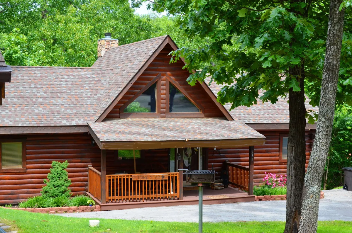This cozy log cabin exterior features a welcoming front porch, landscaped garden, and large windows. The inviting setting is surrounded by nature, suggesting a relaxing retreat for both guests and their pets, with easy access to nearby trails and outdoor activities.