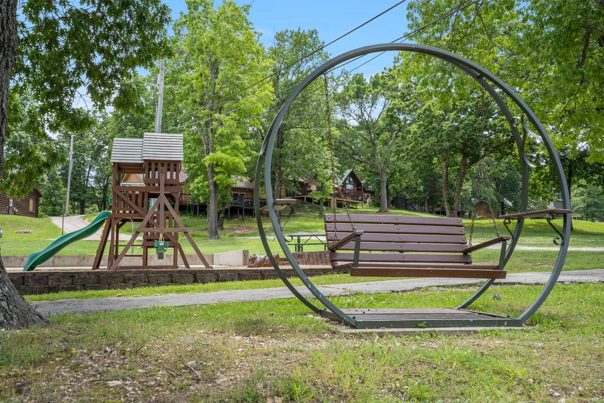 A playful playground scene with a unique circular swing, a sturdy playground structure, and surrounding trees. Cabins are visible in the background, emphasizing the family-friendly, community-oriented atmosphere.