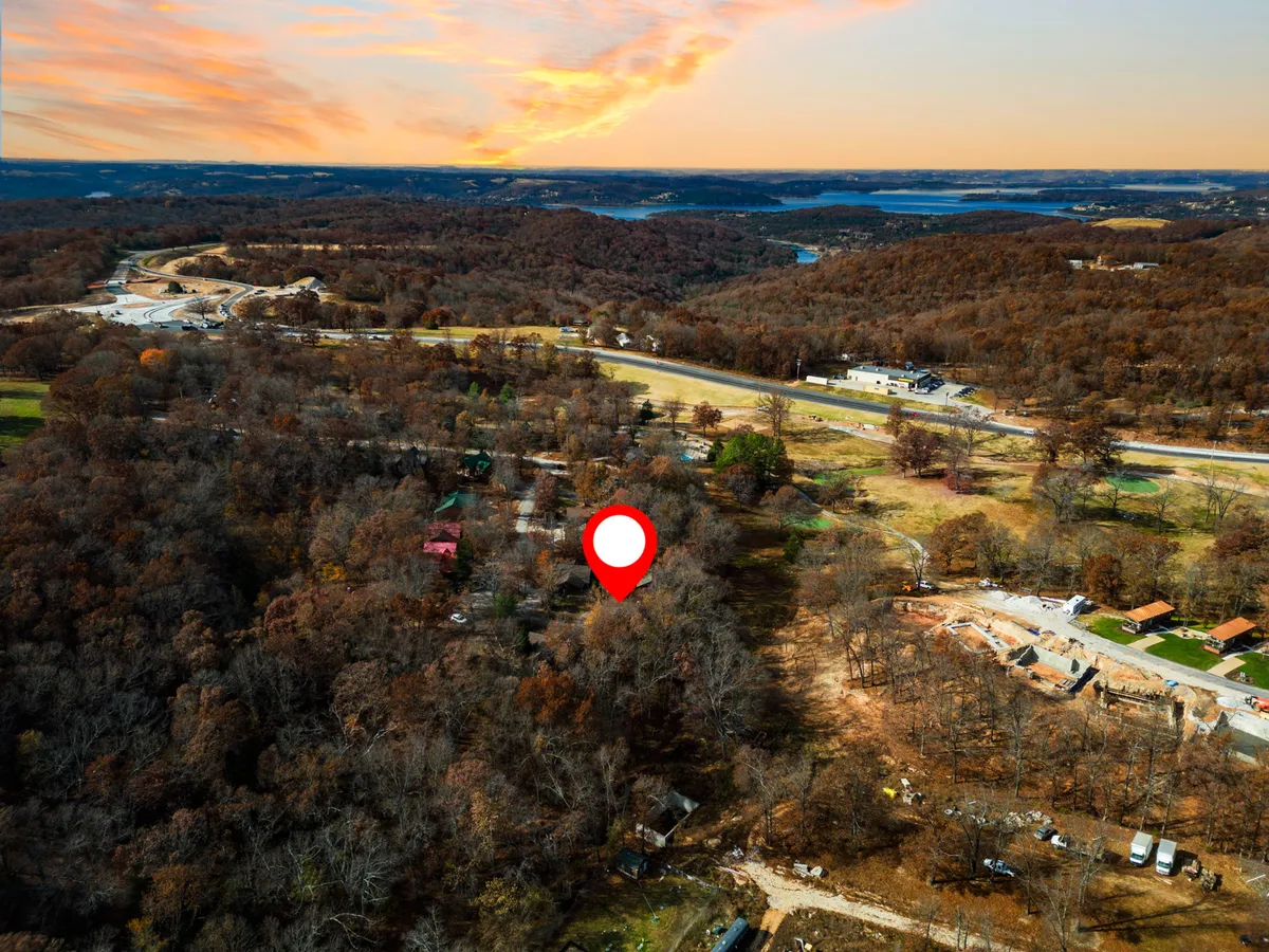 An expansive view shows rolling hills, scattered residential structures, a highway, and a distant lake. The wide perspective captures the natural landscape and accessible location, illustrating the area’s serene environment yet closeness to main roads and attractions.