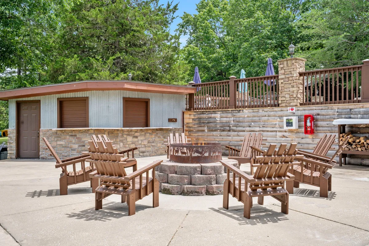 This exterior image highlights a fire pit area with Adirondack chairs arranged on a wooden deck, framed by a stone wall. The space is designed for cozy gatherings, storytelling, and stargazing under the Ozark sky.