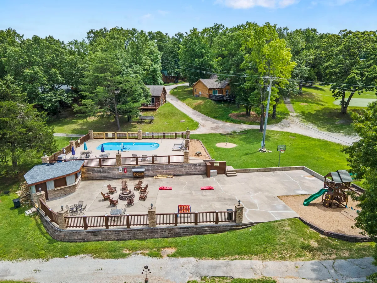This exterior image showcases a swimming pool surrounded by comfortable seating, a playground, and a basketball hoop. Lush greenery frames the area, and the scene is bright and welcoming, clearly inviting families to relax, play, and enjoy various activities together.