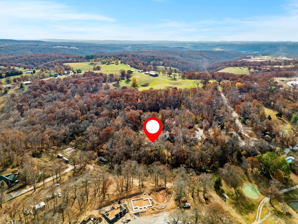 A sweeping vista of rolling hills covered in dense forest, with patches of autumn foliage and scattered residential structures visible in the distance. The view radiates tranquility and showcases the vast, natural beauty of the Ozark region.