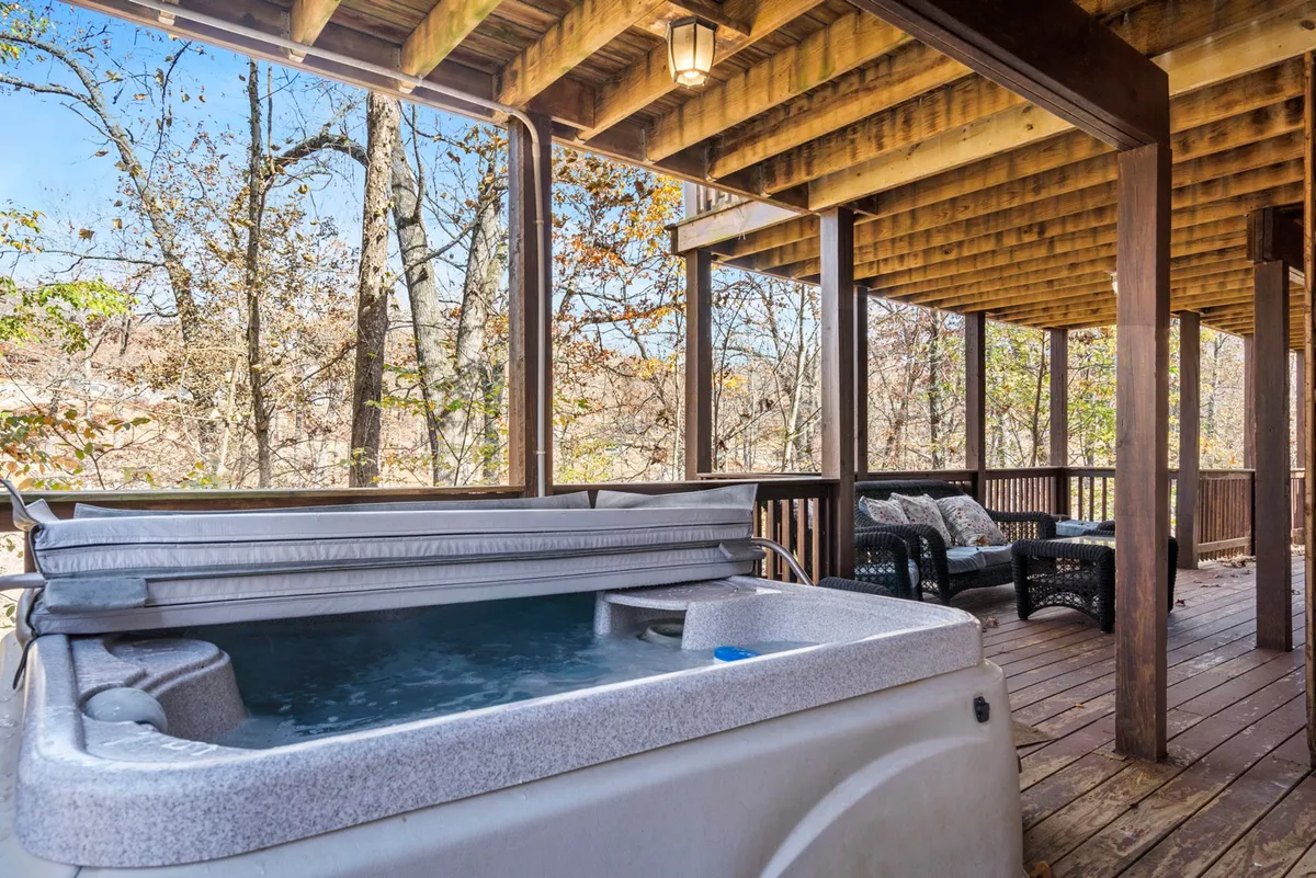 A cozy outdoor deck with a private hot tub and seating area, all nestled within natural surroundings. The space is perfect for unwinding after a day of adventure, with views of the peaceful woods.