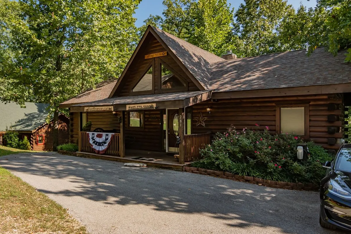 This exterior image spotlights the log cabin structure, its entrance porch, and a decorative star. The scene conveys a warm, welcoming vibe and hints at the cabin's connection to nature and neighborhood amenities.